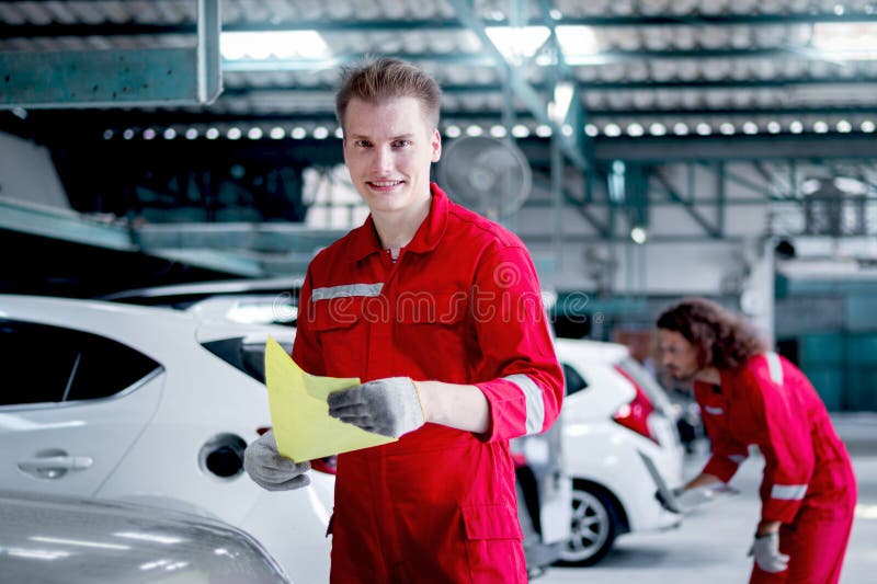 Retrato de un hombre mecánico sonriente con uniforme rojo sujetando la cuenta de pie alrededor de los coches de los coches en el t fotos de archivo libres de regalías