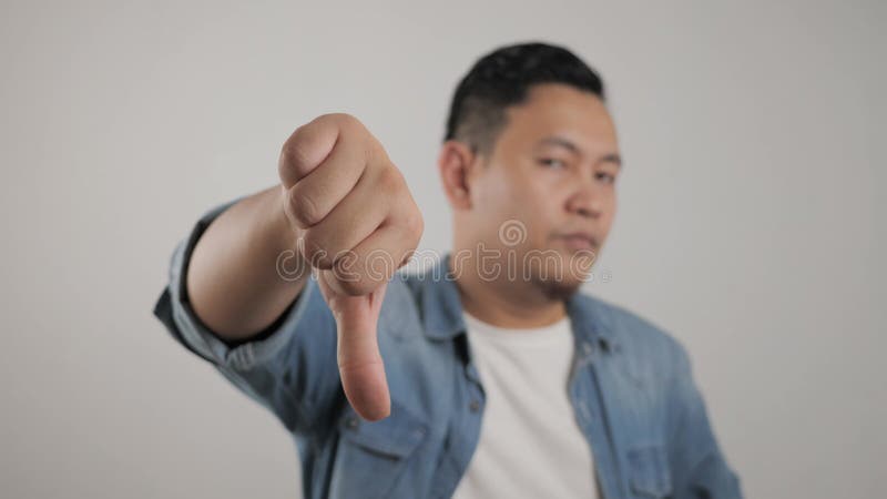 Retrato de un joven asiático muestra expresión de disgusto con pulgares hacia abajo almacen de metraje de vídeo