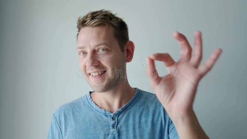 Retrato de un joven caucásico sonriente mostrando un gesto correcto mientras se pone de pie y mira la cámara. alegre tipo feliz almacen de metraje de vídeo
