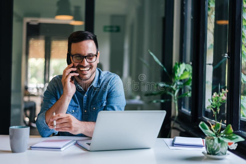 Retrato de un joven y alegre empresario sonriente en una oficina informal haciendo llamadas telefónicas mientras trabaja con una
