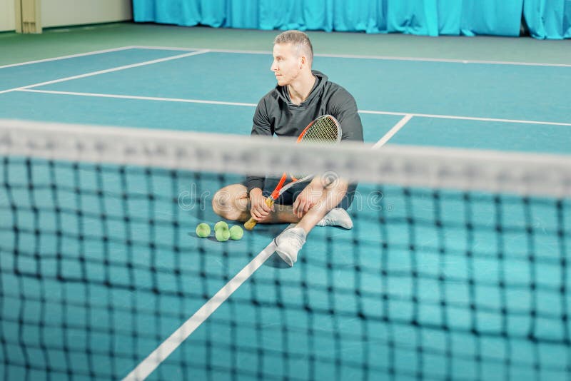 Retrato de un jugador de tenis de sexo masculino individuo joven con una estafa en sus manos que se sientan en la corte fotos de archivo Retrato de un jugador de tenis de sexo masculino individuo joven con una estafa en sus manos que se sientan en la corte fotos de archivo