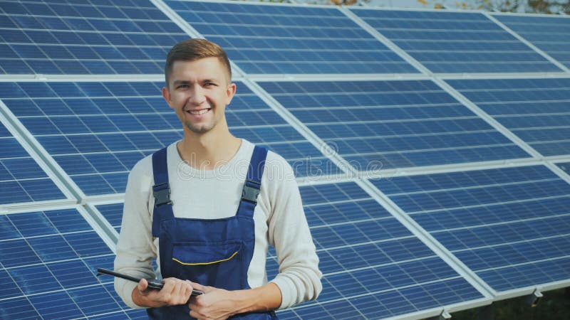 Retrato de un trabajador joven en workwear, sonriendo y mirando la cámara Contra la perspectiva de los paneles solares fotos de archivo libres de regalías Retrato de un trabajador joven en workwear, sonriendo y mirando la cámara Contra la perspectiva de los paneles solares fotos de archivo libres de regalías