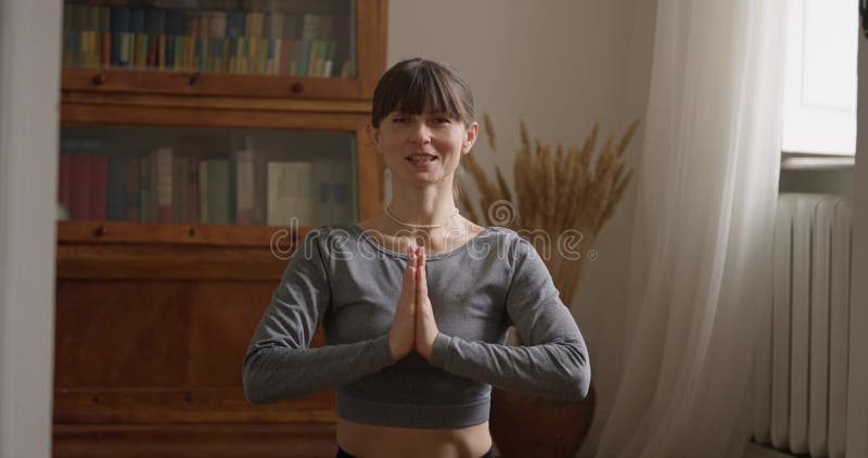 Retrato de una chica con un suéter gris que está meditando y doblando sus manos en una pose de oración en casa. Niña meditando almacen de metraje de vídeo