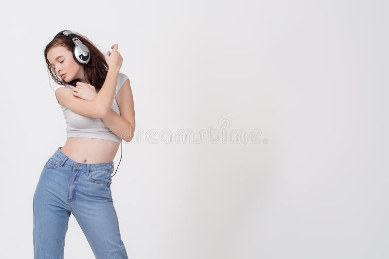 Retrato de una chica joven con el pelo oscuro rizado y auriculares que escucha la música contra el fondo blanco imagen de archivo Retrato de una chica joven con el pelo oscuro rizado y auriculares que escucha la música contra el fondo blanco imagen de archivo