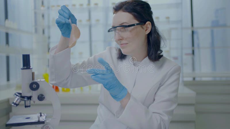 Retrato de una científica con un abrigo blanco con pinzas en las manos mirando la carne cultivada artificialmente de un petri