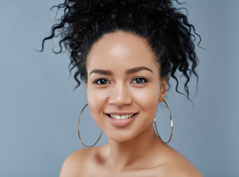 Retrato de una hembra sonriente con pelo rizado y pendientes mirando la cámara fotografía de archivo libre de regalías