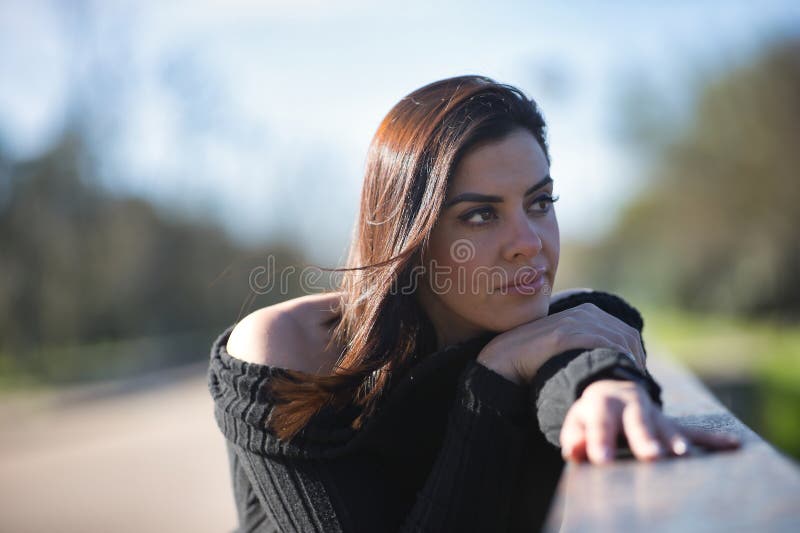 Retrato de una joven hermosa mujer con traje de salto negro con una apariencia soñada y distraída frente a una baranda. concepto imagen de archivo