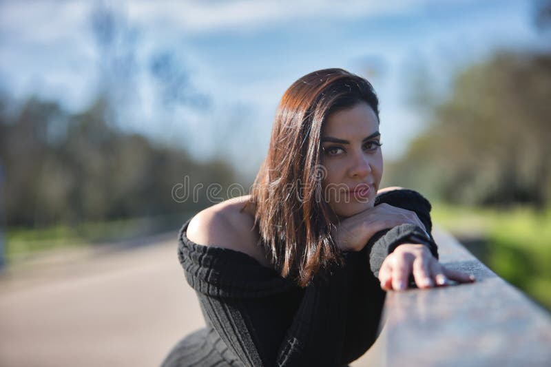 Retrato de una joven hermosa mujer con traje de salto negro mirando a la cámara relajada y tranquila inclinándose contra una baran imagen de archivo