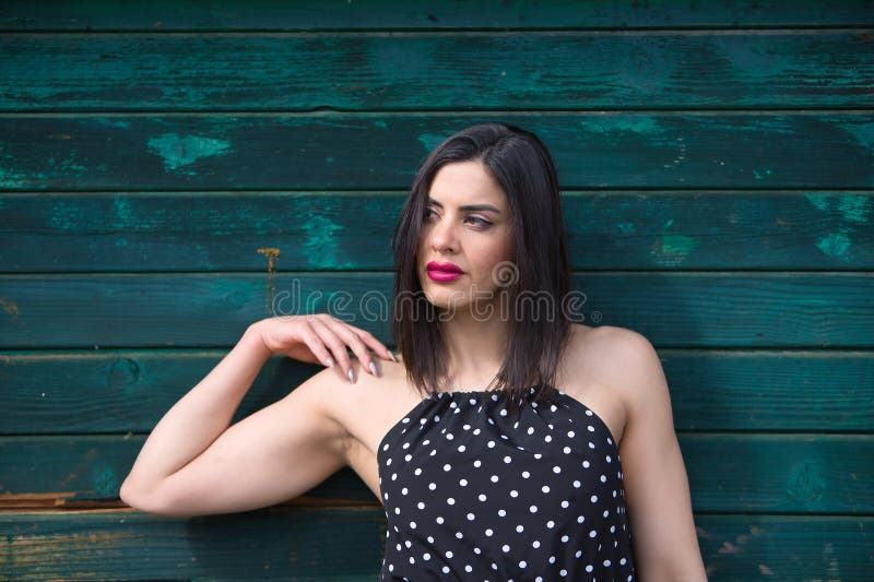 Retrato de una joven hermosa mujer con un vestido negro con puntos de polka blanco que se ve distraída e independiente y con poder fotos de archivo libres de regalías