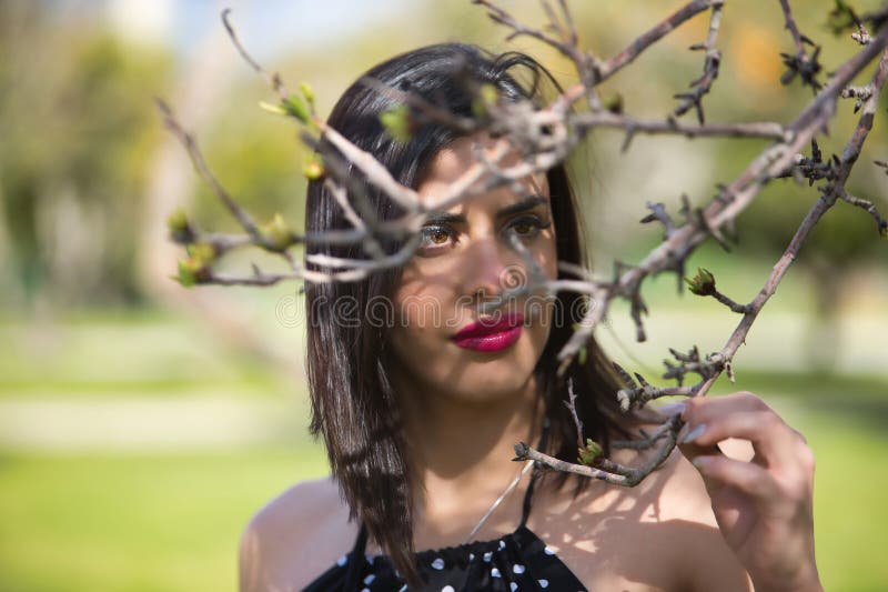 Retrato de una joven linda mujer con un vestido negro con puntos de polka blanco mirando a la cámara a través de las ramas de un á imagen de archivo