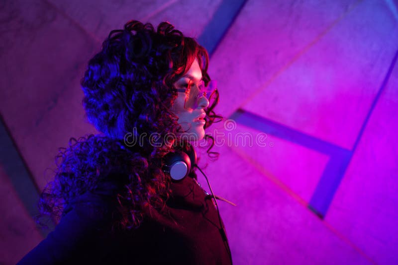 Retrato de una joven mujer sensual curridiza en grandes audífonos, sacada de la cabeza, y sombras, sobre fondo de neón fotografía de archivo