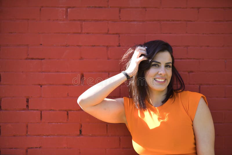 Retrato de una joven y bonita mujer con un vestido naranja con una sonrisa perfecta feliz y sonriente sobre un fondo de ladrillos fotos de archivo libres de regalías