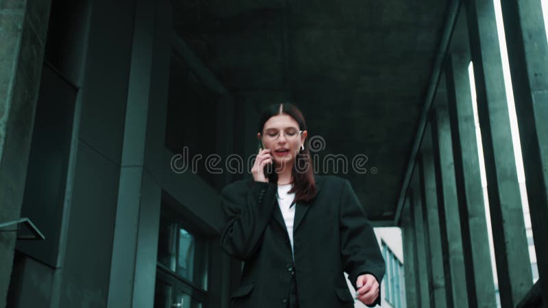 Retrato de una joven y hermosa estudiante de negocios con gafas de traje caminando por la ciudad hablando por teléfono