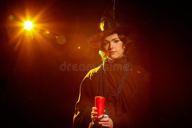 Retrato de una linda bruja joven con un sombrero puntiagudo con la varita de la vela en sus manos y fondo negro. niña o mujer en foto de archivo libre de regalías