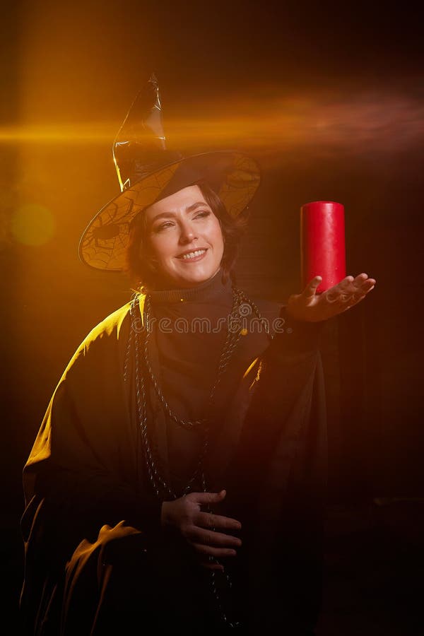Retrato de una linda bruja joven con un sombrero puntiagudo con la varita de la vela en sus manos y fondo negro. niña o mujer en imagen de archivo
