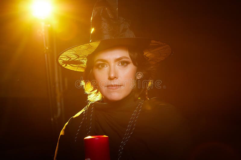 Retrato de una linda bruja joven con un sombrero puntiagudo con la varita de la vela en sus manos y fondo negro. niña o mujer en imagen de archivo libre de regalías