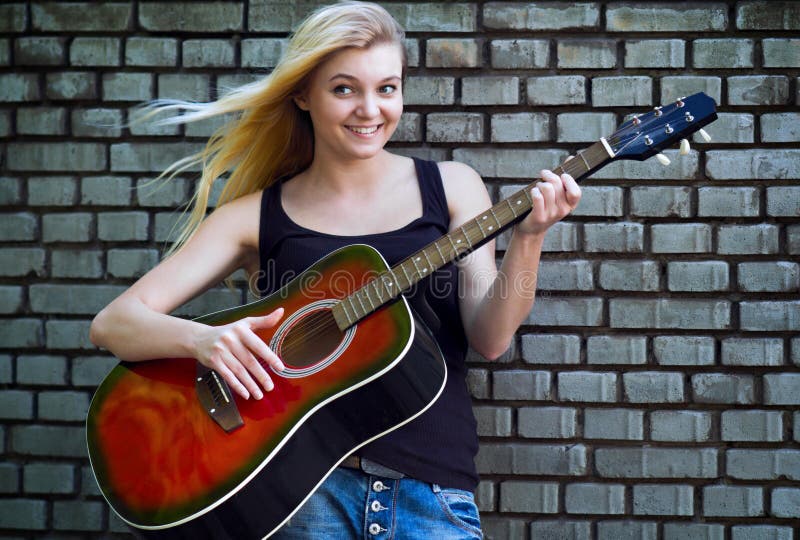Retrato de una mujer con una guitarra cerca de la pared de ladrillo imagen de archivo Retrato de una mujer con una guitarra cerca de la pared de ladrillo imagen de archivo