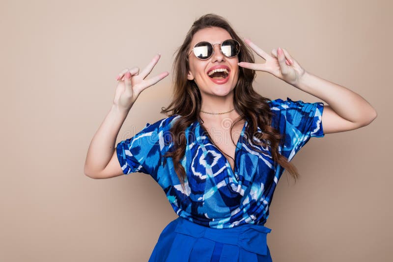Retrato de una mujer feliz sonriente del playfull en las gafas de sol que muestran la muestra de la victoria y que miran la cámar fotos de archivo Retrato de una mujer feliz sonriente del playfull en las gafas de sol que muestran la muestra de la victoria y que miran la cámar fotos de archivo