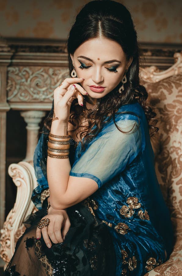 Portrait of a beautiful woman in Indian traditional Chinese dress, with her hands painted with henna mehendi. Girl sitting on a luxury sofa. Portrait of a beautiful woman in Indian traditional Chinese dress, with her hands painted with henna mehendi. Girl sitting on a luxury sofa.