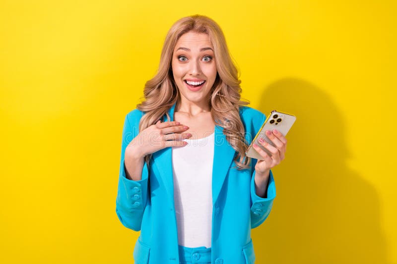 Portrait of positive impressed lady hold smart phone arm touch chest unexpected news isolated on yellow color background. Portrait of positive impressed lady hold smart phone arm touch chest unexpected news isolated on yellow color background.