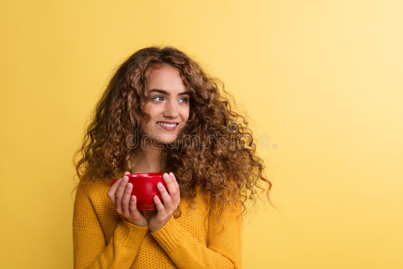 Retrato de una mujer joven con la taza roja en un estudio en un fondo amarillo imagen de archivo Retrato de una mujer joven con la taza roja en un estudio en un fondo amarillo imagen de archivo