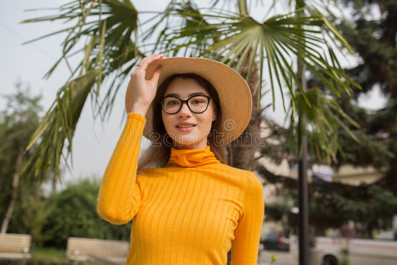 Retrato de una mujer joven en la ciudad Palmeras en el fondo Mujer brillante feliz con el sombrero de los vidrios i imagenes de archivo Retrato de una mujer joven en la ciudad Palmeras en el fondo Mujer brillante feliz con el sombrero de los vidrios i imagenes de archivo