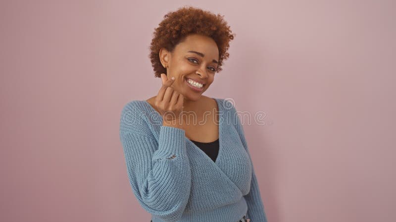 Retrato de una mujer negra sonriente con el pelo rizado en un fondo rosado con un suéter azul imagen de archivo libre de regalías