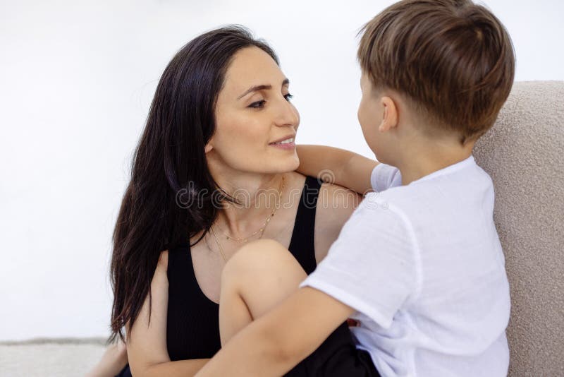 Retrato de una mujer sonriente abrazando a un niño en casa. Madre y su hijo con ropa informal están sentados en el sofá foto de archivo libre de regalías