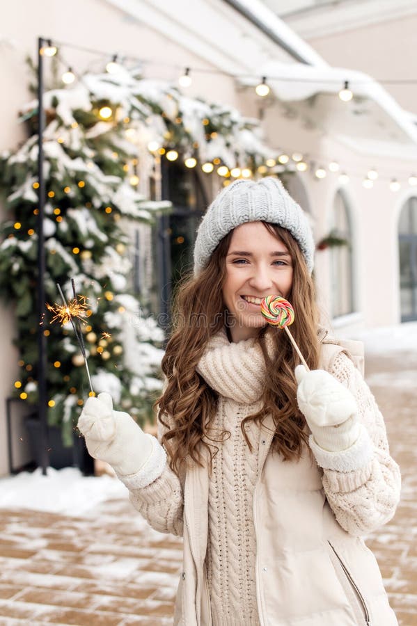 Retrato de una niña feliz con un dulce caminando en la ciudad en invierno. Niña feliz sosteniendo chispas y comiendo caramelos afuera en invierno