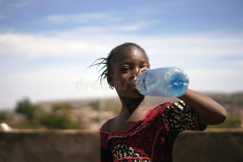 Retrato de una pequeña niña africana que bebe codiciosamente de una botella de agua foto de archivo