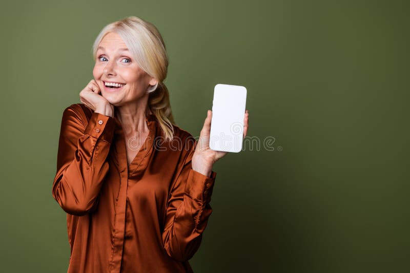 Portrait of impressed person with blond hair wear blouse presenting online store on smartphone display isolated on khaki color background. Portrait of impressed person with blond hair wear blouse presenting online store on smartphone display isolated on khaki color background.