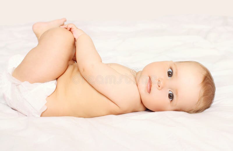 Retrato del bebé lindo en los pañales que mienten en la cama foto de archivo Retrato del bebé lindo en los pañales que mienten en la cama foto de archivo