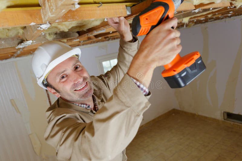 Retrato del constructor masculino usando taladro inalámbrico en viga de madera imágenes de archivo libres de regalías