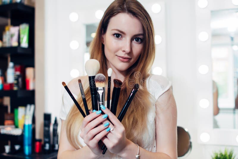 Retrato del cosmetólogo femenino que sostiene un sistema de cepillos del maquillaje en salón de belleza imagenes de archivo Retrato del cosmetólogo femenino que sostiene un sistema de cepillos del maquillaje en salón de belleza imagenes de archivo