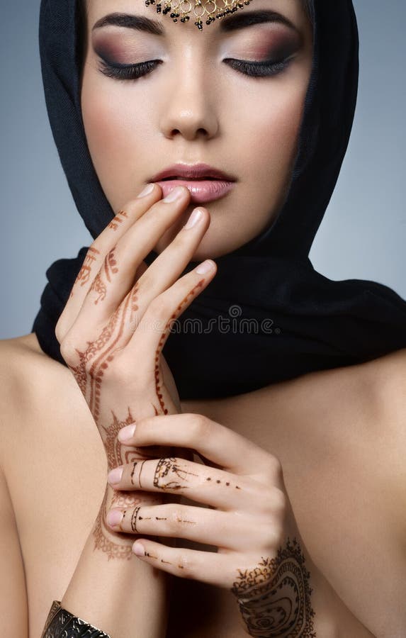Beautiful fashion east woman portrait.Asian girl in a black headscarf tenderly toucheszbeautiful slender fingers to his lips. East girl with henna tattoos.Hindu model with perfect make-up.India.Asia. Beautiful fashion east woman portrait.Asian girl in a black headscarf tenderly toucheszbeautiful slender fingers to his lips. East girl with henna tattoos.Hindu model with perfect make-up.India.Asia