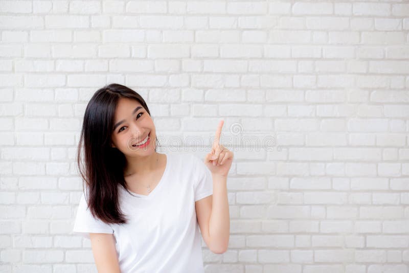 Retrato del finger derecho de la felicidad asiática joven hermosa de la mujer que señala algo en textura gris del cemento