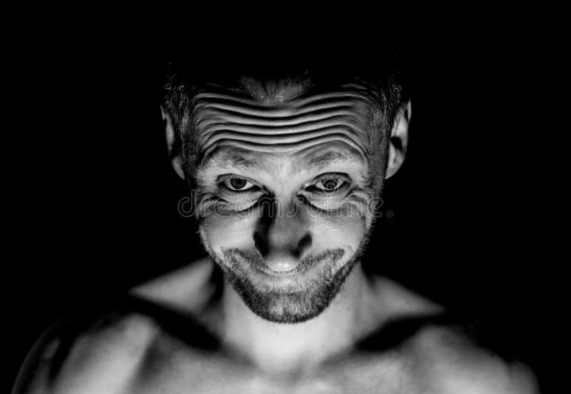 Retrato del hombre caucásico adulto sin afeitar Él sonríe como maniaco y parece como locura Tiro blanco y negro, iluminación disc foto de archivo