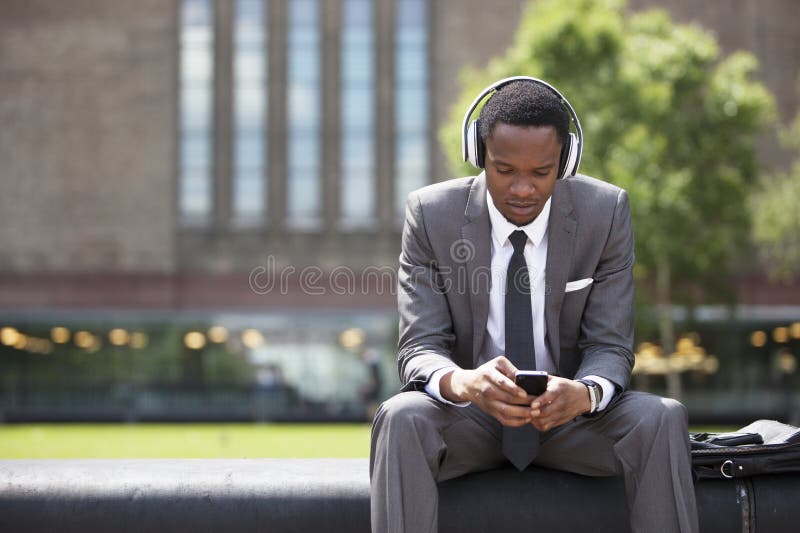 Retrato del hombre de negocios afroamericano que escucha la música con los auriculares al aire libre