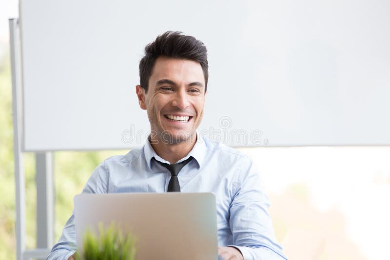 Retrato del hombre de negocios joven que sonríe y que trabaja con el ordenador portátil en la oficina, imagen de archivo Retrato del hombre de negocios joven que sonríe y que trabaja con el ordenador portátil en la oficina, imagen de archivo