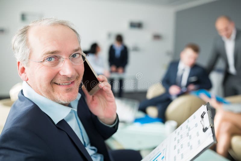 Retrato del hombre de negocios mayor sonriente Talking On Smartphone adentro imagenes de archivo Retrato del hombre de negocios mayor sonriente Talking On Smartphone adentro imagenes de archivo