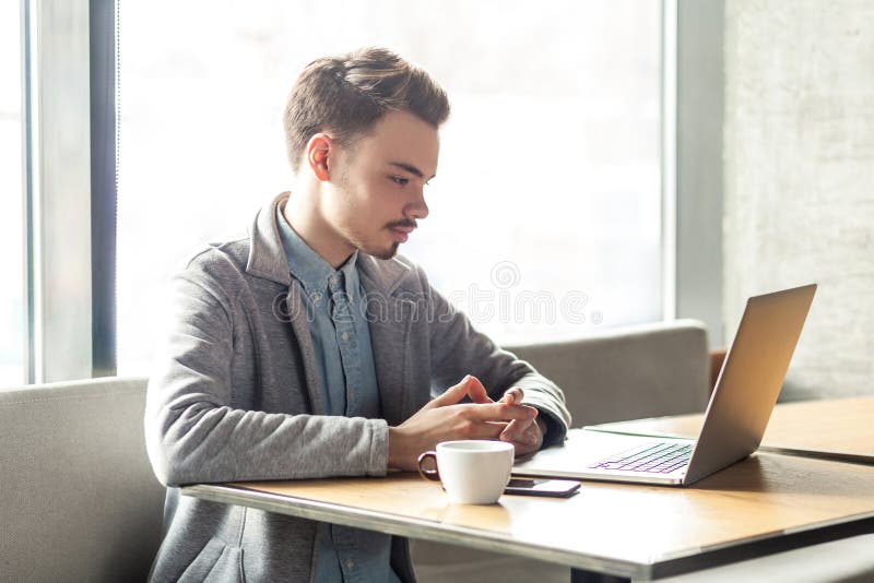 Retrato del hombre de negocios serio acertado joven que trabaja en el ordenador que se sienta en oficina fotos de archivo libres de regalías Retrato del hombre de negocios serio acertado joven que trabaja en el ordenador que se sienta en oficina fotos de archivo libres de regalías