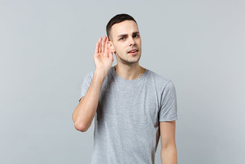 Retrato del hombre joven curioso en la ropa casual que mira la mano de la tenencia de la audiencia de la cámara cerca del oído ai imagenes de archivo Retrato del hombre joven curioso en la ropa casual que mira la mano de la tenencia de la audiencia de la cámara cerca del oído ai imagenes de archivo