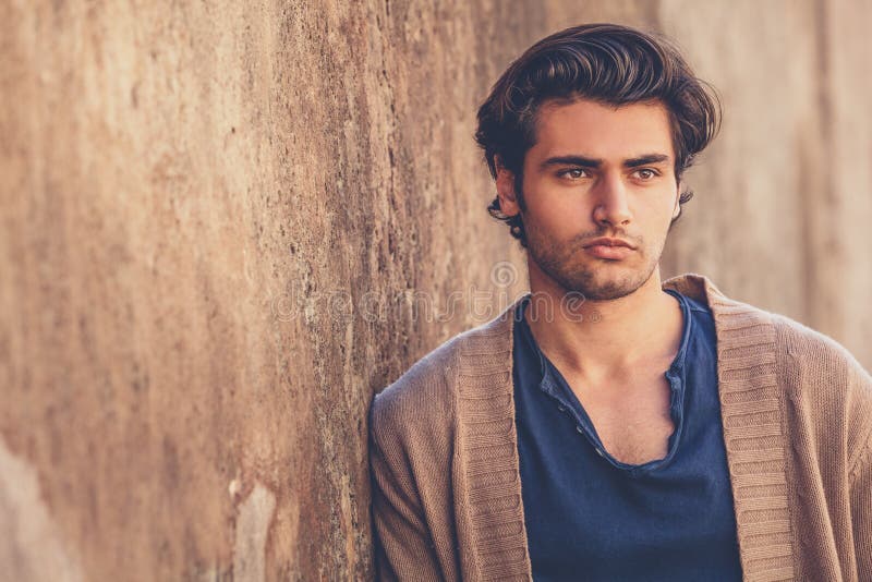 Retrato del hombre joven hermoso y encantador Él se está inclinando contra una pared al aire libre imagen de archivo libre de regalías