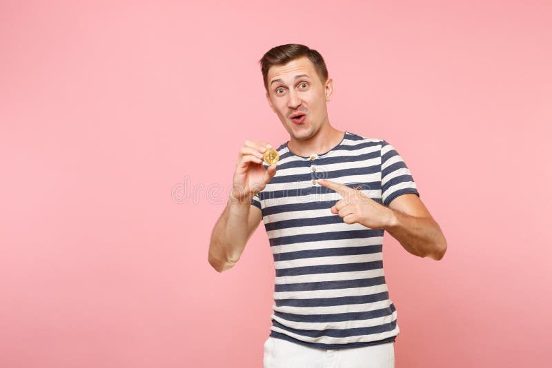 Retrato del hombre joven sonriente en la camiseta rayada que lleva a cabo el bitcoin, moneda del metal del color de oro aislada e fotos de archivo libres de regalías