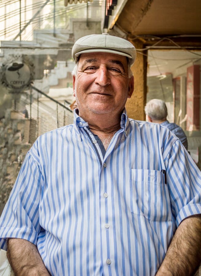 Retrato del hombre mayor feliz que lleva la camisa rayada azul y el casquillo plano imagen de archivo libre de regalías Retrato del hombre mayor feliz que lleva la camisa rayada azul y el casquillo plano imagen de archivo libre de regalías