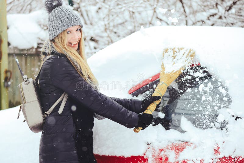 Retrato del invierno de una nieve de la limpieza de la mujer joven de un coche La belleza Girl modelo rubio ríe y limpia alegre l foto de archivo libre de regalías Retrato del invierno de una nieve de la limpieza de la mujer joven de un coche La belleza Girl modelo rubio ríe y limpia alegre l foto de archivo libre de regalías