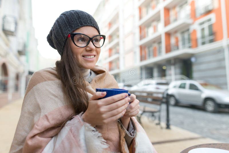 Retrato del invierno del otoño de la mujer sonriente joven en sombrero, con la taza de bebida caliente Fondo de la calle de la ci imagen de archivo Retrato del invierno del otoño de la mujer sonriente joven en sombrero, con la taza de bebida caliente Fondo de la calle de la ci imagen de archivo
