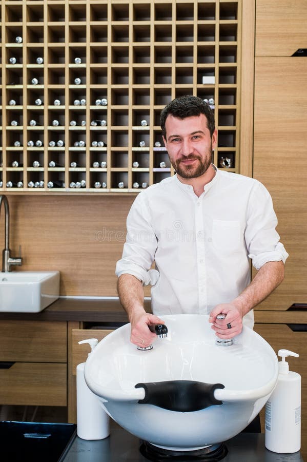 Retrato del peluquero feliz con el golpecito de agua cerca del fregadero en la barbería del salón foto de archivo Retrato del peluquero feliz con el golpecito de agua cerca del fregadero en la barbería del salón foto de archivo