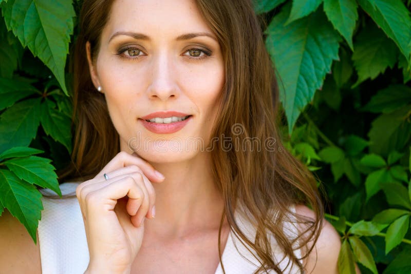 Retrato del primer de la mujer morena hermosa joven en fondo de las hojas foto de archivo