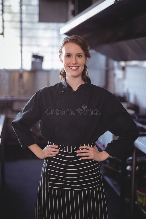 Retrato do barista fêmea novo de sorriso que está com mãos no quadril na cozinha fotos de stock Retrato do barista fêmea novo de sorriso que está com mãos no quadril na cozinha fotos de stock
